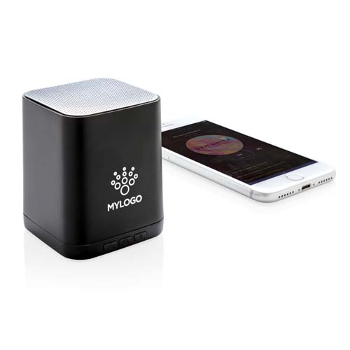 Altavoz Bluetooth cuadrado negro con logotipo personalizado junto a un smartphone reproduciendo música